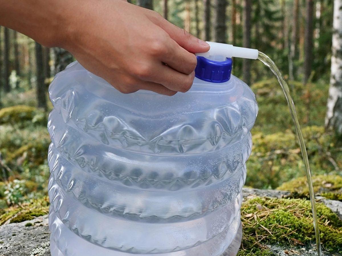 Hands filling a collapsible Trygghetslagret water container in a forest